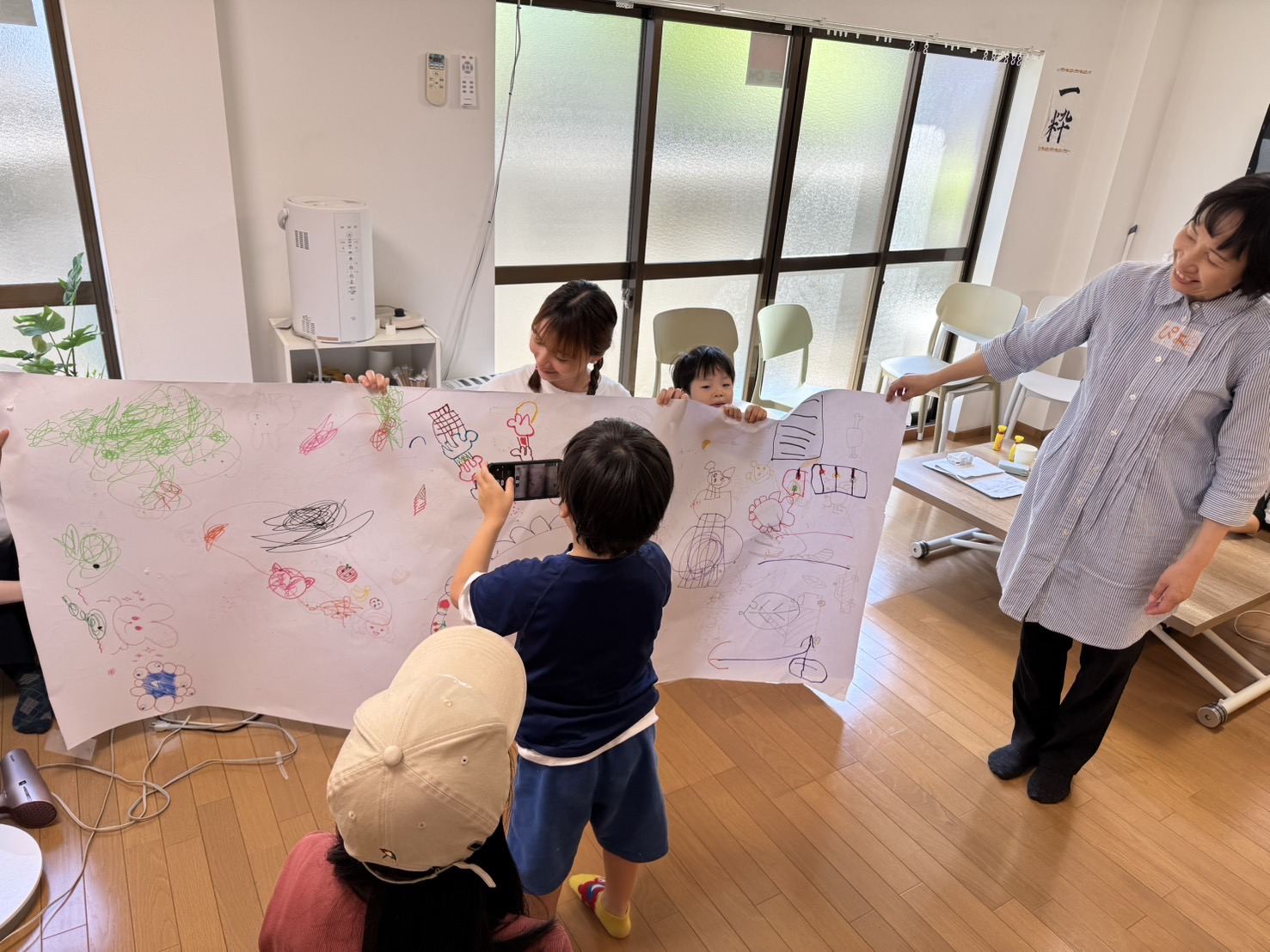 大きな紙にみんなで描いた絵を広げている子どもたちとスタッフ